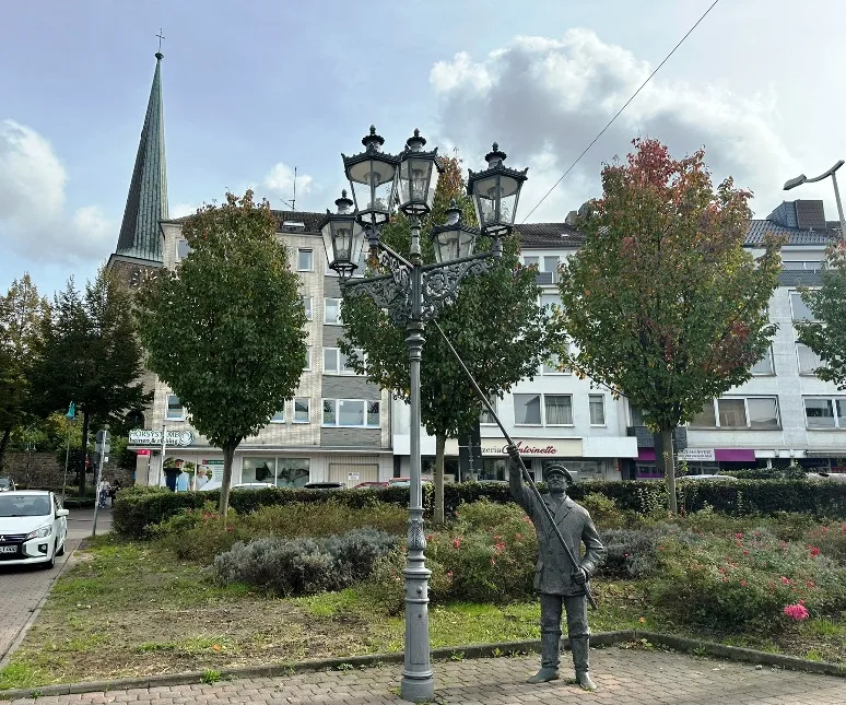 Mülheim an der Ruhr Geschichte: Bronze-Skulptur in Mülheim an der Ruhr mit der historischen Altstadt und der Petrikirche im Hintergrund. Die Statue steht im Vordergrund, während die mittelalterliche Architektur die Szene vervollständigt.