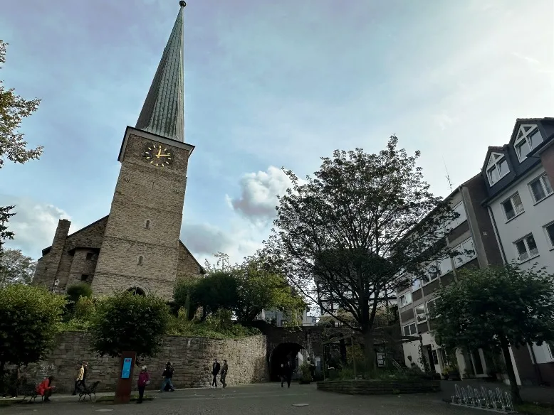 Das Tor zur Altstadt von Mülheim an der Ruhr mit der Petrikirche auf der linken Seite. Rechts befinden sich restaurierte Fachwerkhäuser, die die historische Atmosphäre der Altstadt betonen.