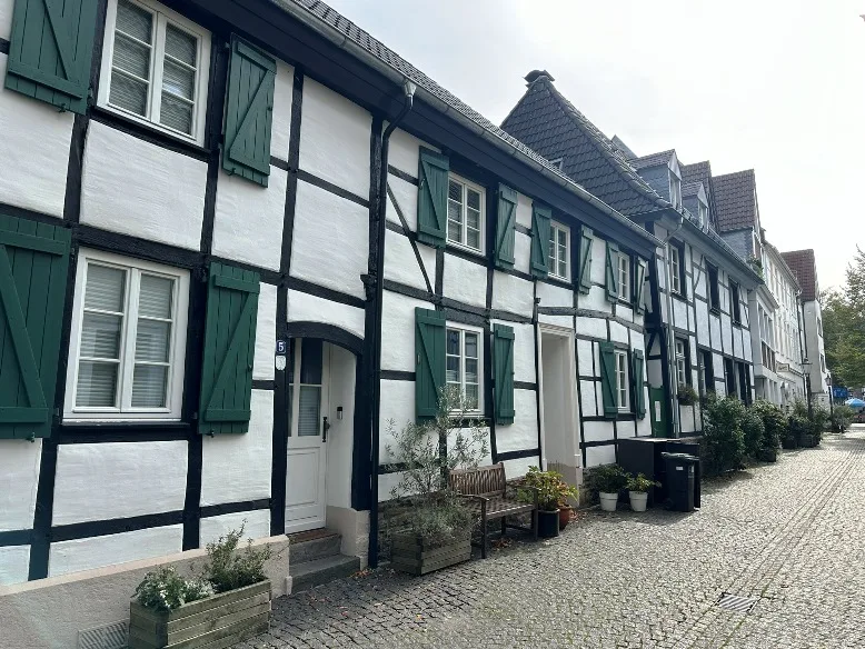  Kopfsteinpflasterstraße in der Altstadt von Mülheim an der Ruhr, gesäumt von traditionellen Fachwerkhäusern. Die Szene zeigt den Charme und die historische Bausubstanz des Viertels.