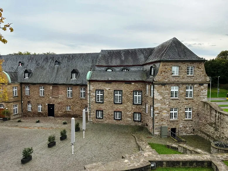 Sehenswürdigkeiten in Mülheim - Innenhof von Schloss Broich in Mülheim an der Ruhr, umgeben von historischen Steinmauern und einer gepflegten Grünanlage, unter einem leicht bewölkten Himmel.